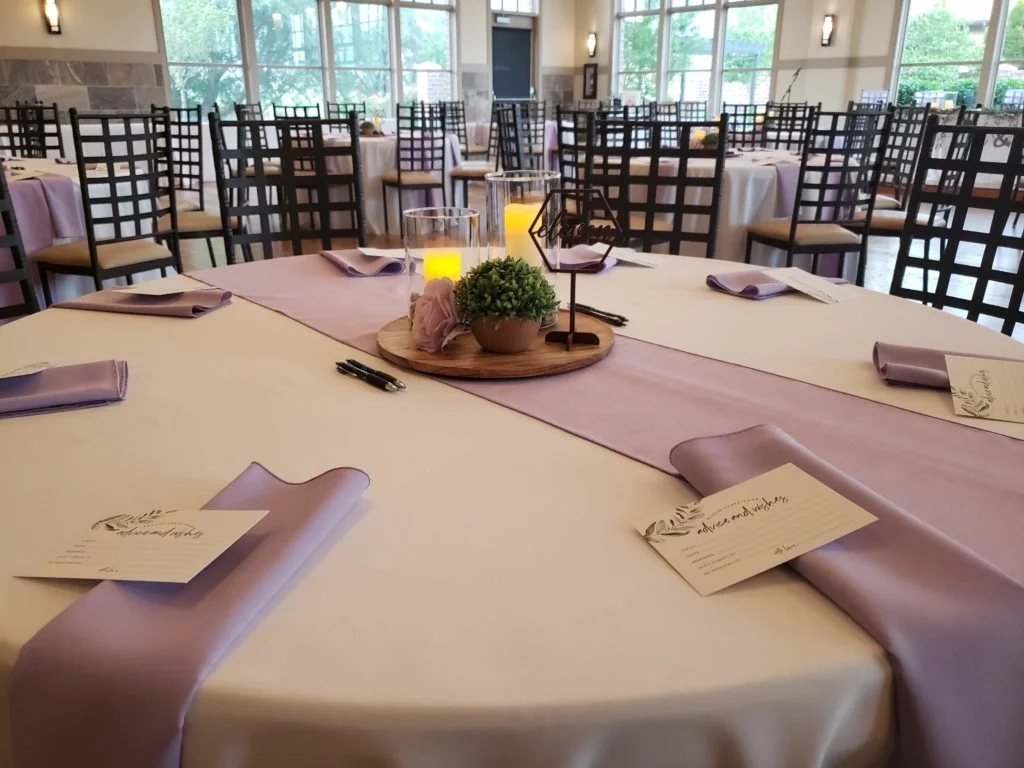 Round reception table set with lavender linens, candles, and a wood centerpiece
